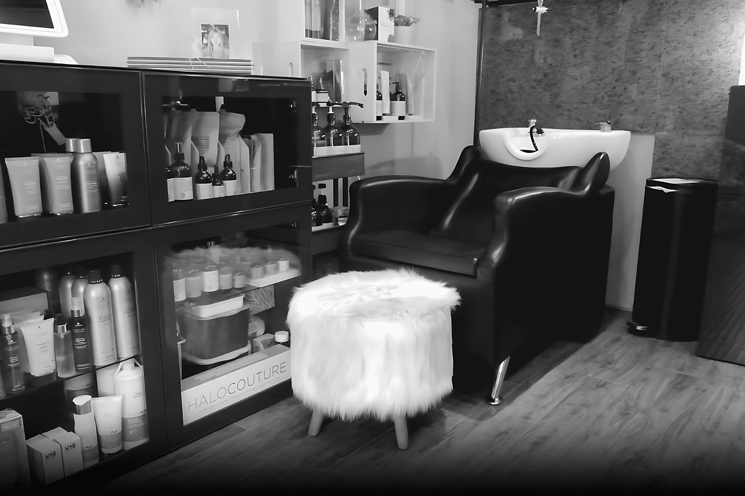 Modern hair salon station with hair products, a black chair, and a white fluffy stool.