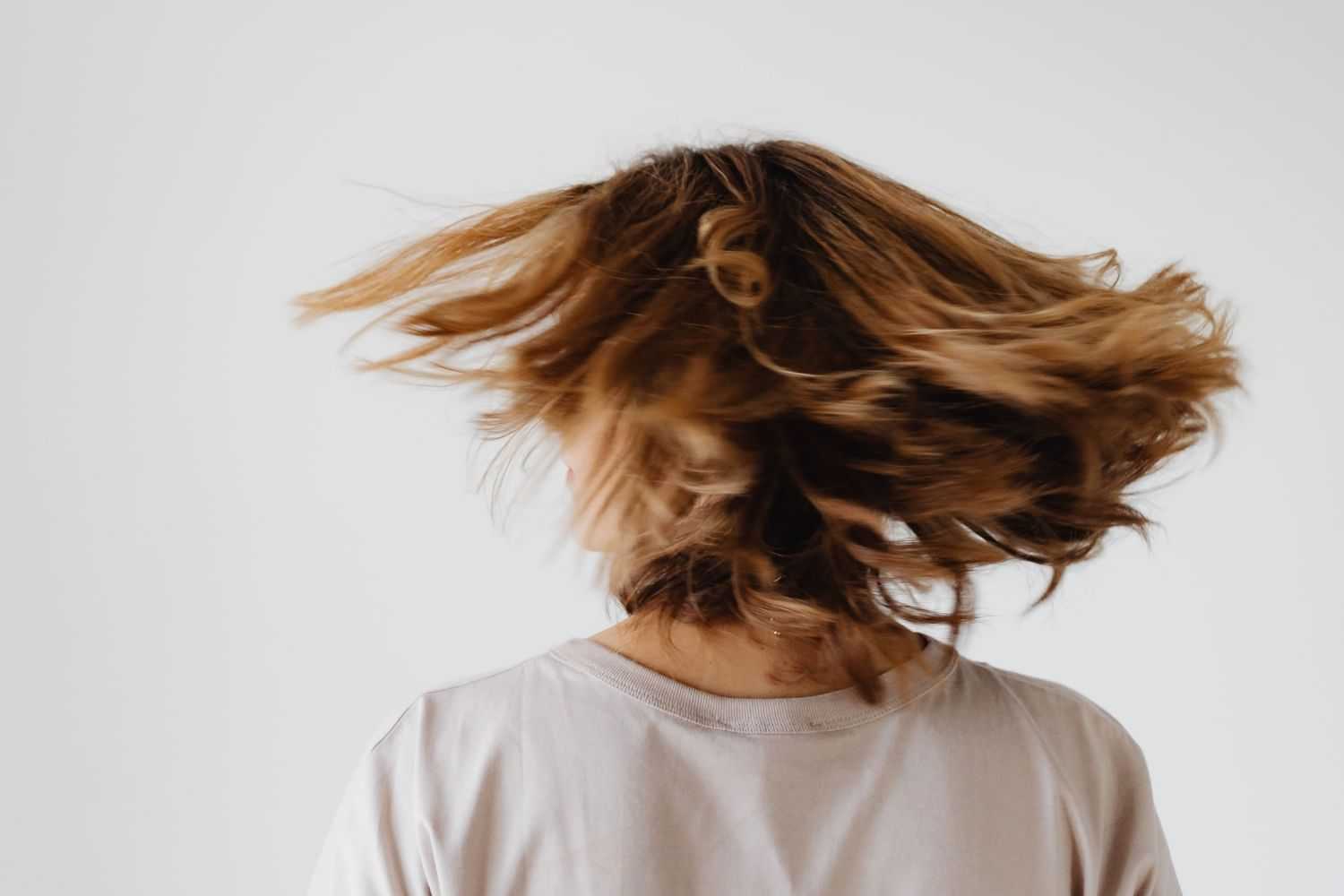Person with tousled hair moving, wearing a light shirt against a plain background.