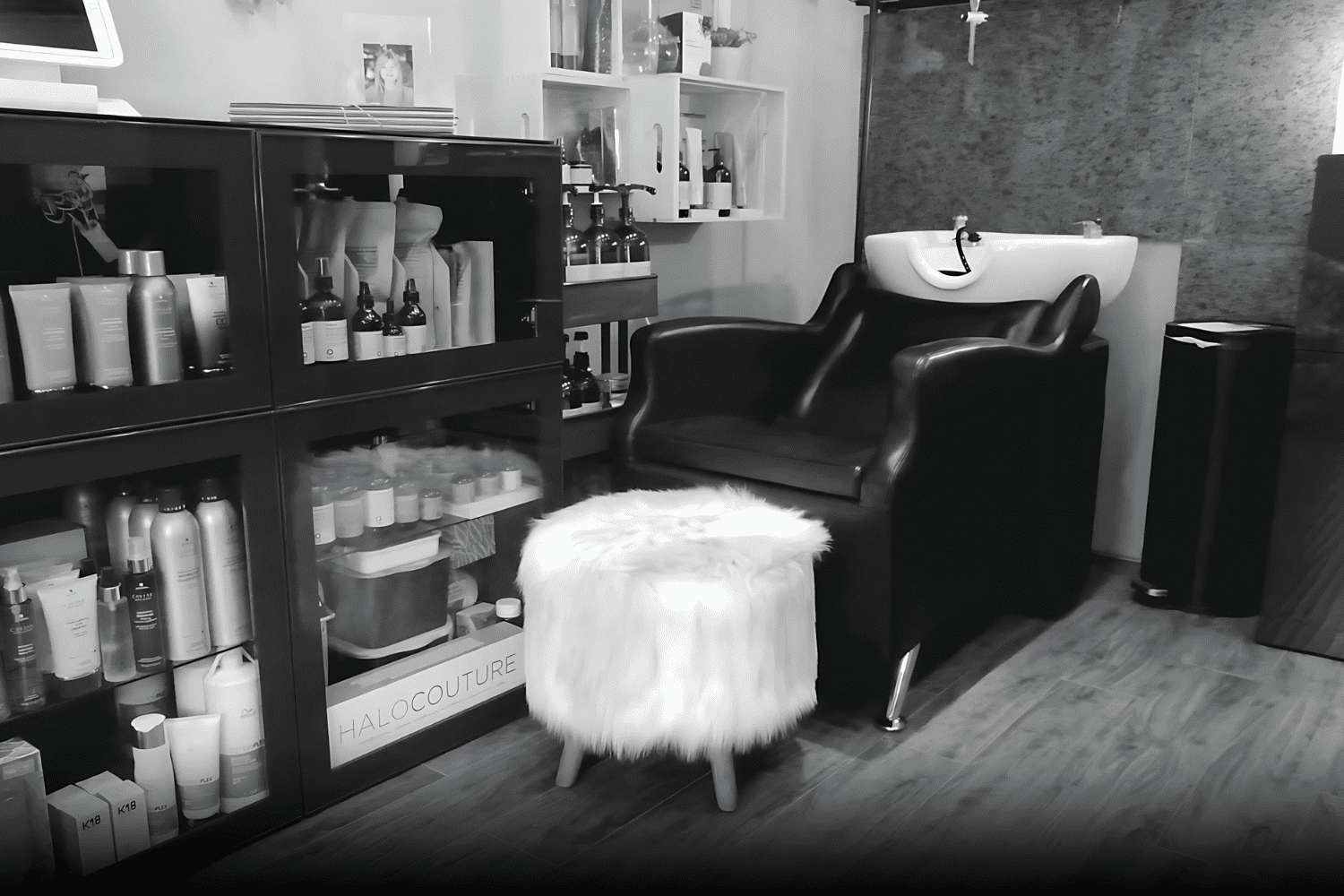 Modern hair salon station with hair products, a black chair, and a white fluffy stool.